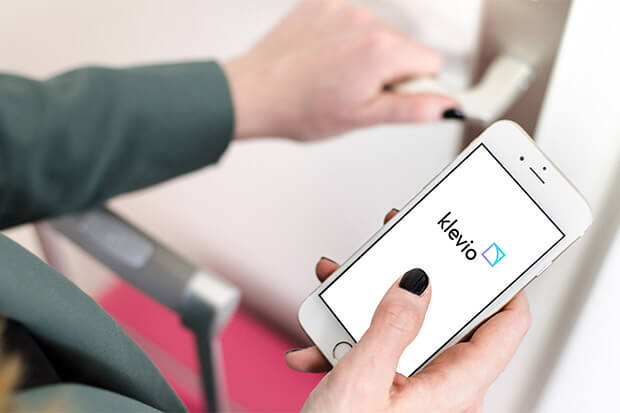A closeup of an Airbnb guest's hands holding a door handle in one hand whilst using their the Klevio app on their smarphone with the other and a suitcase in the background