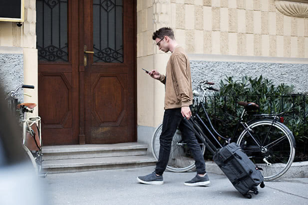 An Airbnb guest walking toward a front door with a suitcase in one hand and a smartphone in the other