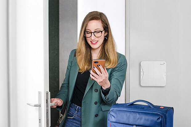 An Airbnb guest coming through a door holding their suitcase and smartphone