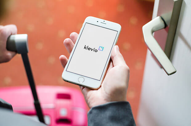 An Airbnb guest's perspective holding a suitcase and the Klevio app on a phone as they enter through a door