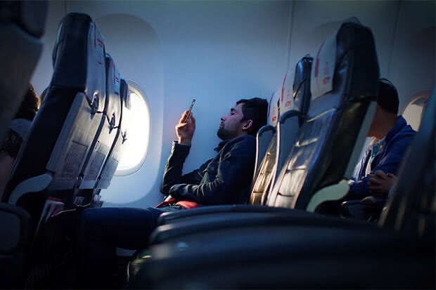 A tired person slouching in a seat on an aeroplane whilst looking at their phone
