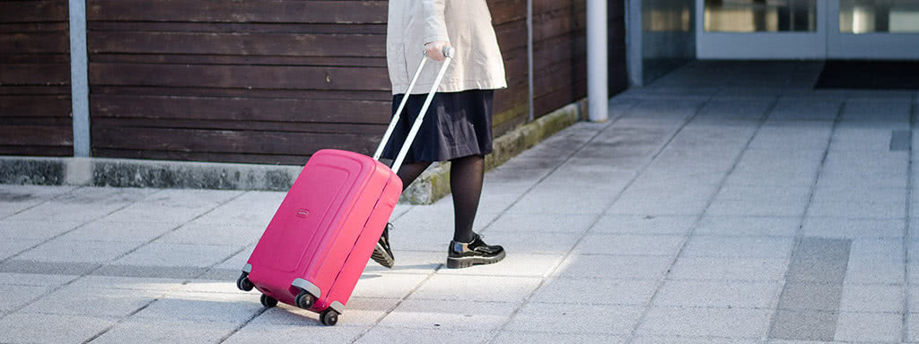 View of a person's legs walking with a pink suitcase