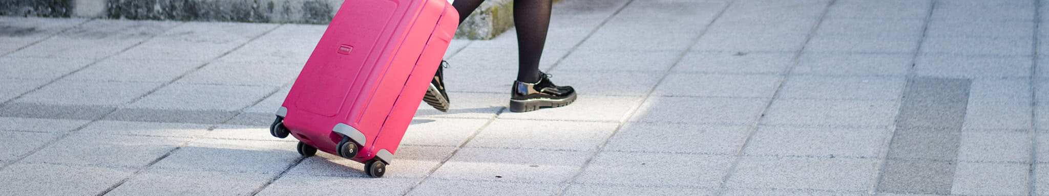 View of a person's legs walking with a pink suitcase