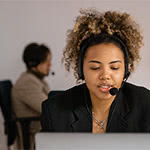 Frontal image of a customer support person talking into her headset and looking down at a laptop screen