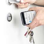 One hand holds a door handle while the other hand holds a phone with the Klevio app and a bunch of physical keys