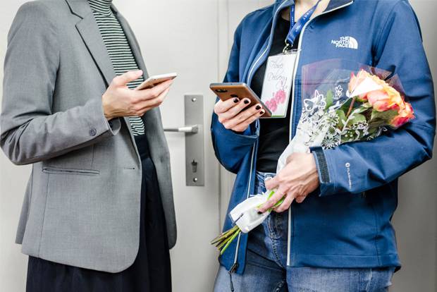 A business woman and delivery person holding smartphones in front of a door