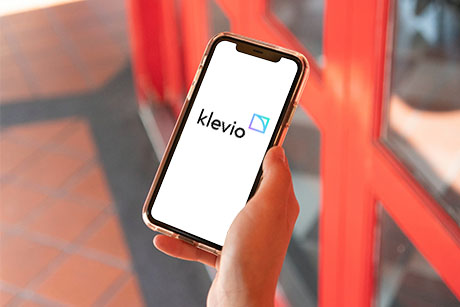 A user holding a smart phone in front of a door with the Klevio app on it