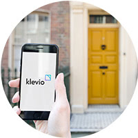 A smartphone with digital keys visible in the Klevio app and a door in the background