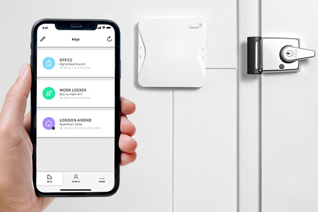 A smartphone with digital keys visible in the Klevio app and a door in the background