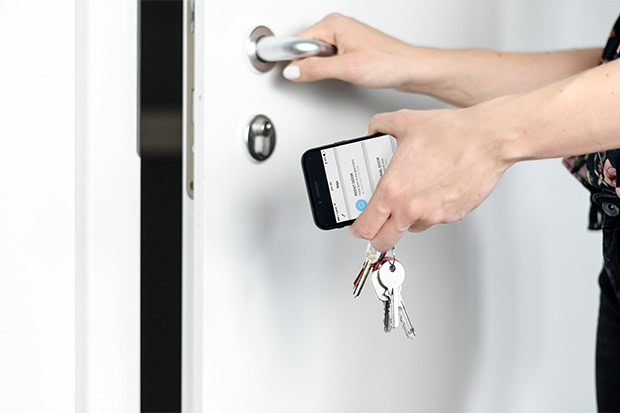 Hands opening a door while holding a smartphone with a smart lock app and physical keys