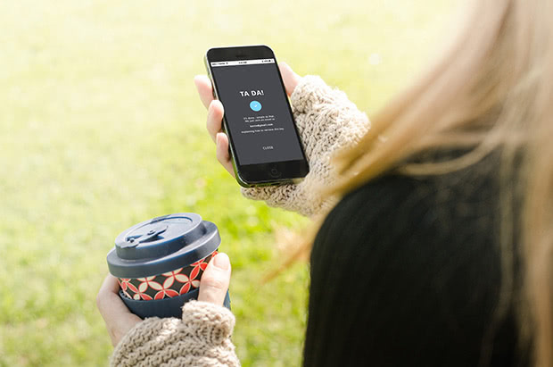 Person standing outside with coffee in one hand and a smartphone in the other, sharing digital keys via a smart lock app