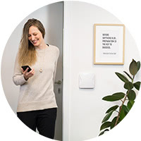 Smart lock user walking through a door into their apartment with a smart lock device on the wall a potted plant on the floor