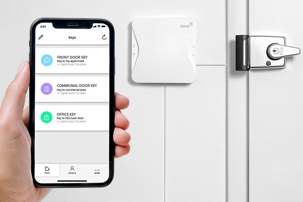 A smartphone with digital keys visible in the Klevio app and a door in the background